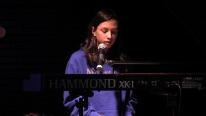 Boy with long dark hair and purple shirt playing the keyboard